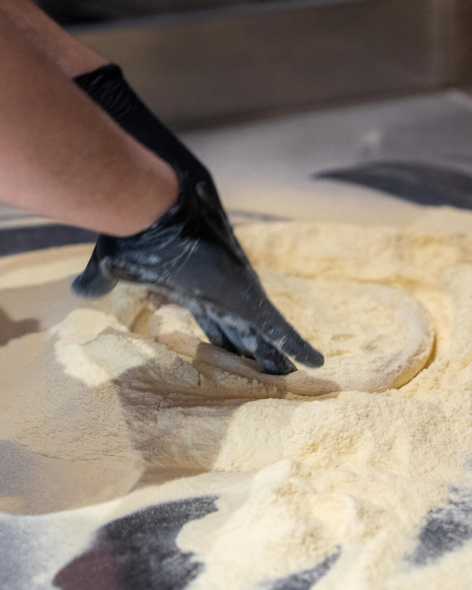 Le mani stendono l'impasto sulla semola
